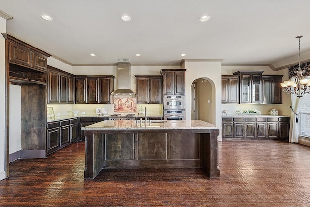 kitchen with a kitchen island with sink, dark brown cabinets, and wall chimney exhaust hood