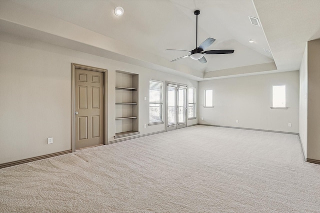 unfurnished living room featuring ceiling fan, light colored carpet, built in shelves, and a tray ceiling