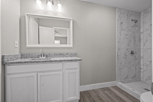 bathroom featuring toilet, vanity, wood-type flooring, and tiled shower