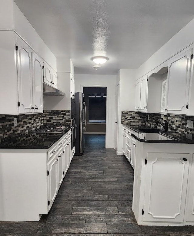 1911 College St, Gainesville, TX 76240 - kitchen with dark countertops, white cabinets, under cabinet range hood, and backsplash