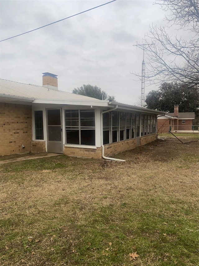1911 College St, Gainesville, TX 76240 - rear view of house with a sunroom, brick siding, a lawn, and a chimney