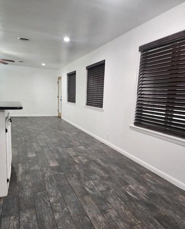 unfurnished living room with a brick fireplace, dark wood-type flooring, and ceiling fan