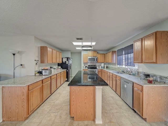 kitchen featuring a textured ceiling, appliances with stainless steel finishes, a kitchen island, sink, and light tile patterned flooring