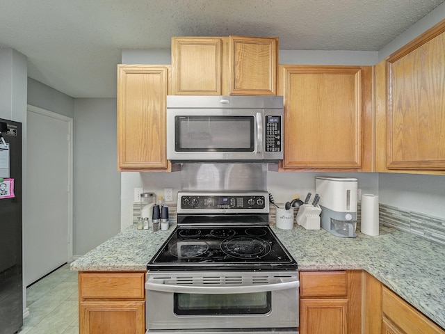 kitchen with light stone counters, light brown cabinetry, stainless steel appliances, and a textured ceiling