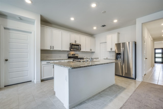 kitchen with decorative backsplash, stainless steel appliances, sink, white cabinetry, and an island with sink