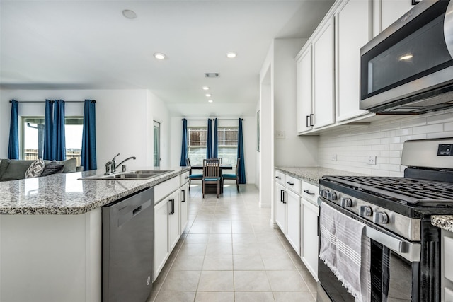 kitchen with light stone countertops, sink, stainless steel appliances, a kitchen island with sink, and white cabinets