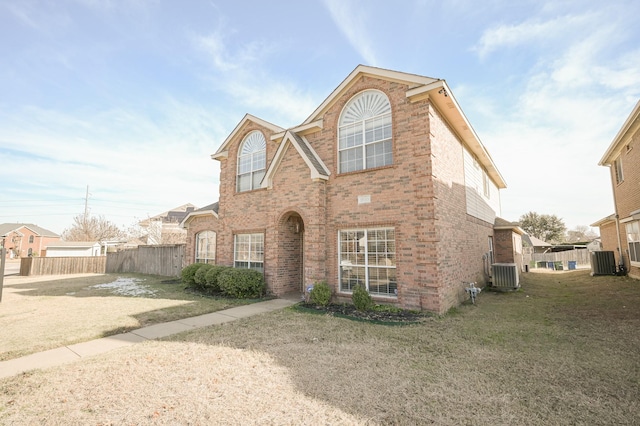 traditional home with a front yard, central air condition unit, fence, and brick siding