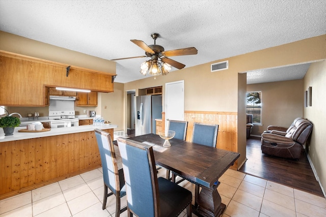 dining room featuring a textured ceiling, ceiling fan, wooden walls, and light tile patterned floors