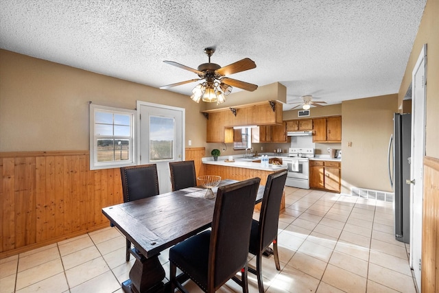 dining space with a textured ceiling, wood walls, light tile patterned flooring, ceiling fan, and sink