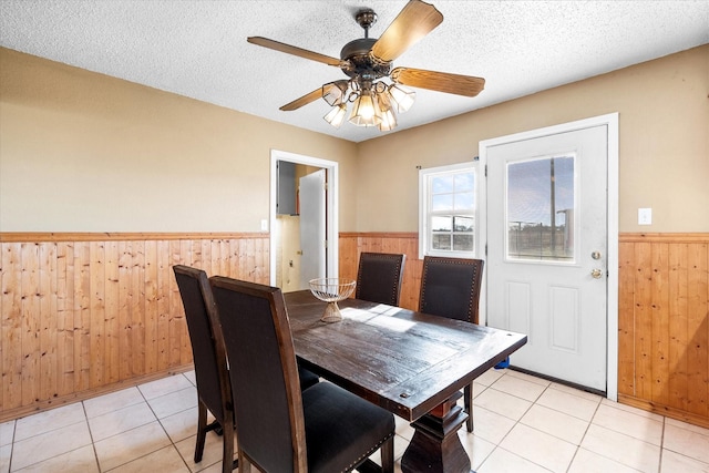 tiled dining room featuring ceiling fan, wooden walls, and a textured ceiling