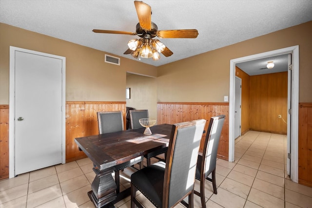 dining space with ceiling fan, wooden walls, a textured ceiling, and light tile patterned floors