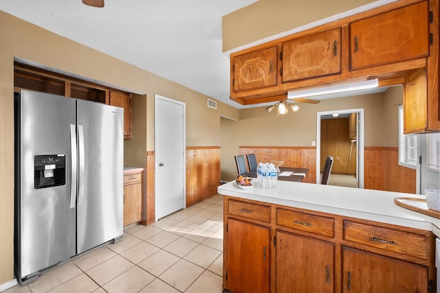 kitchen featuring kitchen peninsula, light tile patterned floors, ceiling fan, wooden walls, and stainless steel refrigerator with ice dispenser