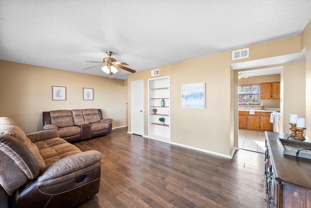 living room with a textured ceiling, ceiling fan, dark hardwood / wood-style flooring, and built in shelves