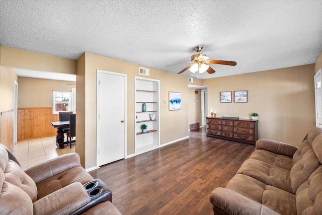 living room with wooden walls, a textured ceiling, hardwood / wood-style floors, ceiling fan, and built in shelves