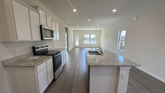 kitchen with light stone countertops, dark hardwood / wood-style floors, a kitchen island with sink, white cabinetry, and appliances with stainless steel finishes