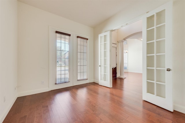 spare room with french doors, decorative columns, and wood-type flooring