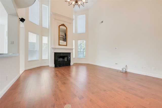 unfurnished living room with a high ceiling, light wood-type flooring, a notable chandelier, and a tiled fireplace