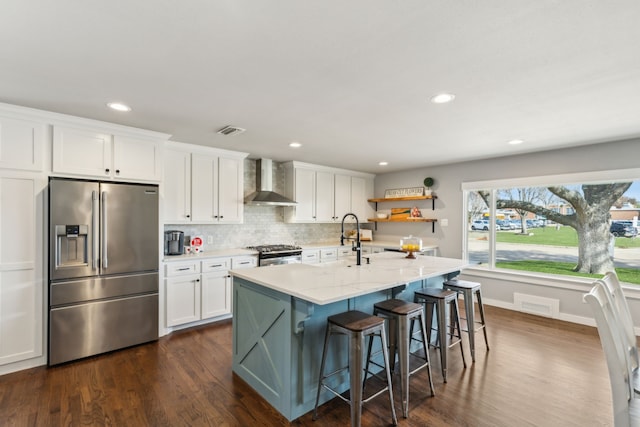 kitchen featuring white cabinets, stainless steel appliances, wall chimney range hood, and a kitchen island with sink