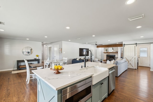 kitchen featuring light stone countertops, a center island with sink, a barn door, appliances with stainless steel finishes, and sink