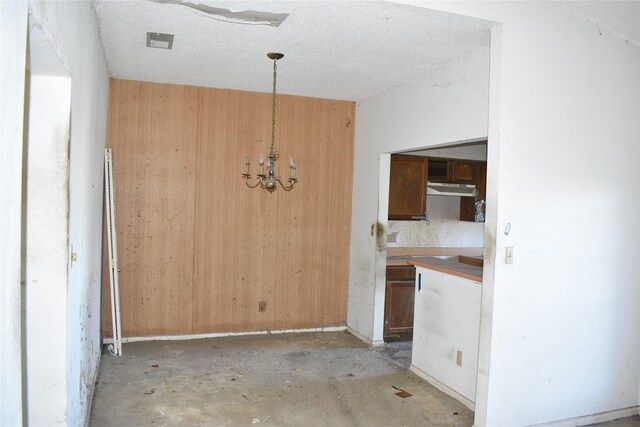 kitchen featuring wooden walls, a textured ceiling, and a notable chandelier