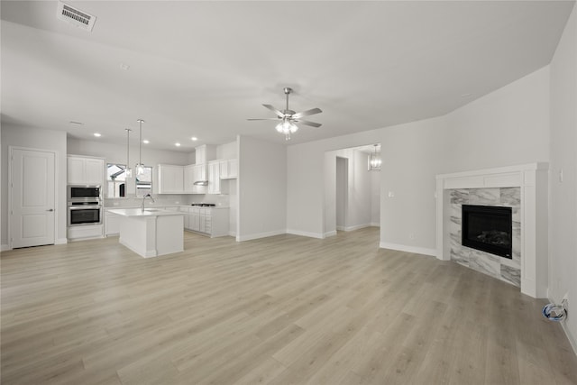 unfurnished living room featuring ceiling fan, a premium fireplace, light hardwood / wood-style flooring, and sink