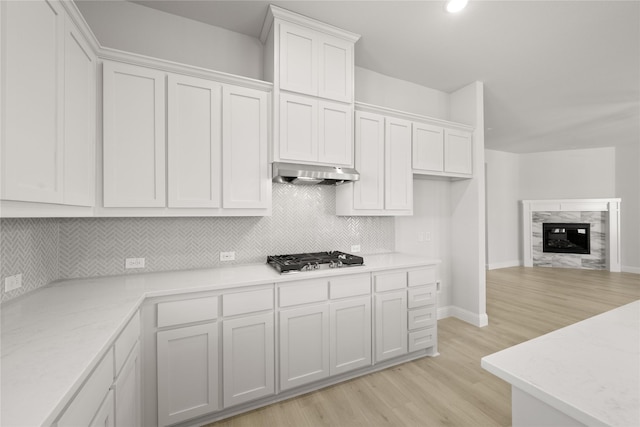 kitchen with white cabinetry, stainless steel gas cooktop, a fireplace, tasteful backsplash, and light hardwood / wood-style flooring