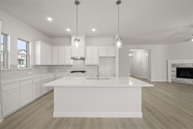 kitchen featuring sink, white cabinetry, pendant lighting, a premium fireplace, and a kitchen island with sink