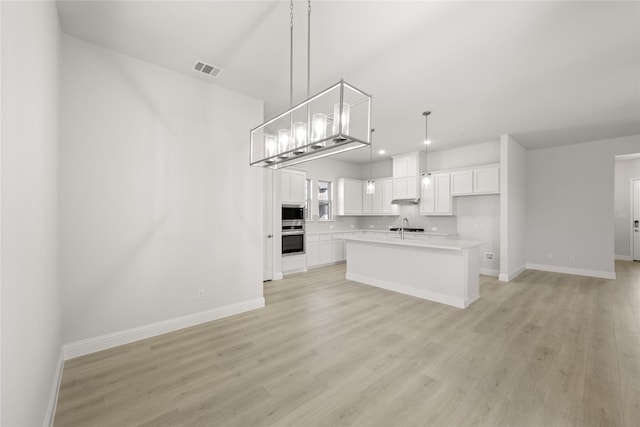 kitchen featuring white cabinets, hanging light fixtures, light wood-type flooring, and a kitchen island with sink