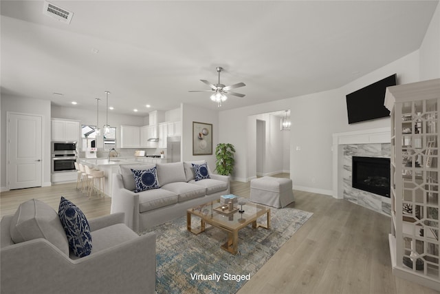 living room with sink, a fireplace, ceiling fan, and light wood-type flooring