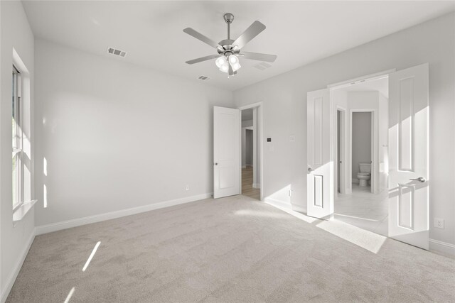 unfurnished bedroom with ensuite bath, light carpet, and ceiling fan