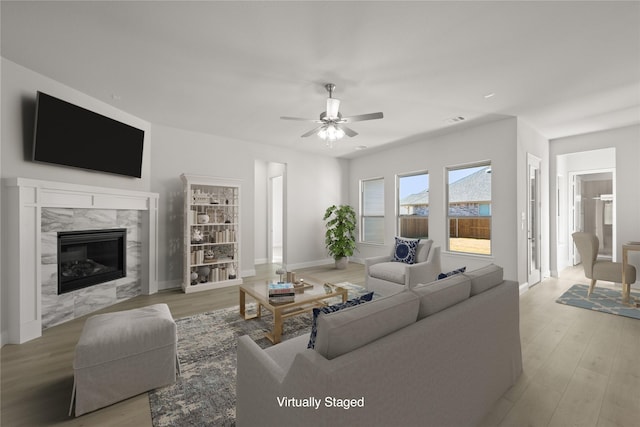 living room with ceiling fan, light wood finished floors, a premium fireplace, and baseboards