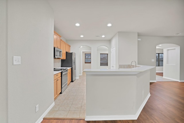 kitchen with light brown cabinetry, an island with sink, stainless steel appliances, and light tile patterned flooring