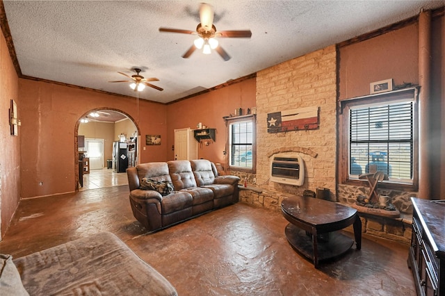 living room featuring ceiling fan, ornamental molding, heating unit, and a textured ceiling