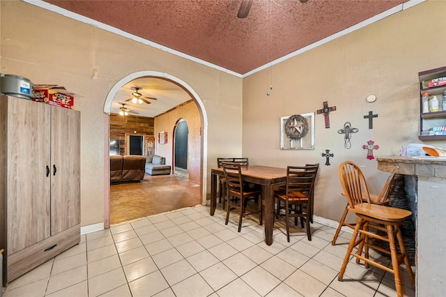 dining area with ceiling fan, crown molding, a textured ceiling, wooden walls, and light tile patterned floors