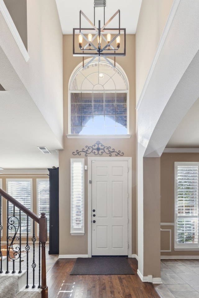 foyer entrance with a notable chandelier, a towering ceiling, plenty of natural light, and dark wood-type flooring