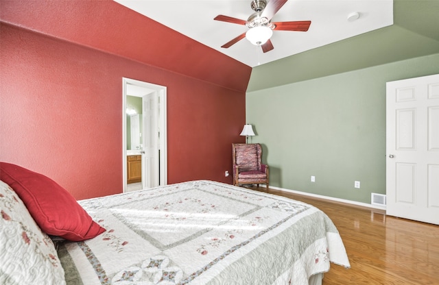 bedroom featuring ceiling fan, hardwood / wood-style floors, vaulted ceiling, and ensuite bathroom