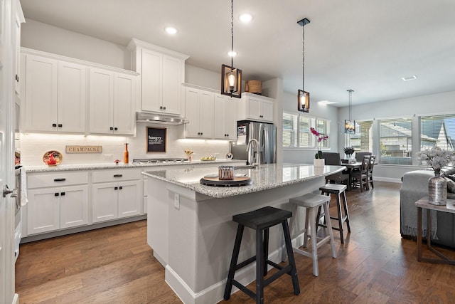 kitchen featuring hanging light fixtures, stainless steel appliances, a kitchen island with sink, white cabinets, and a kitchen breakfast bar