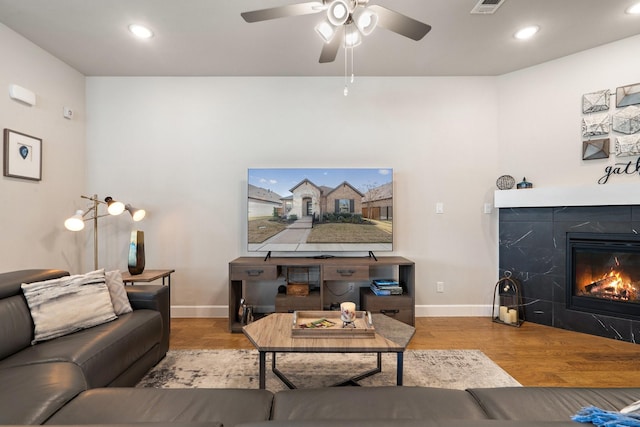 living room with a tiled fireplace, ceiling fan, and wood-type flooring