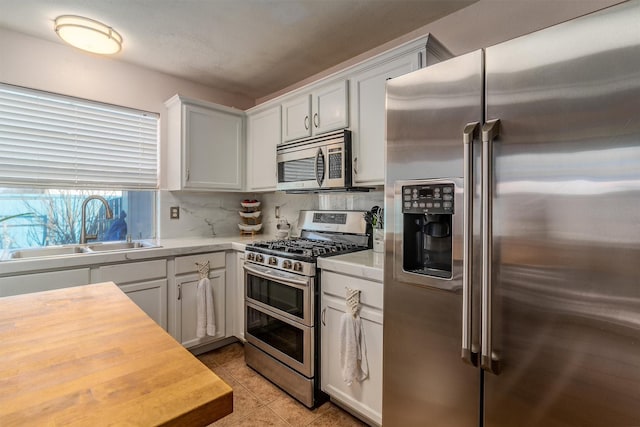 kitchen featuring stainless steel appliances, light tile patterned floors, backsplash, white cabinetry, and sink