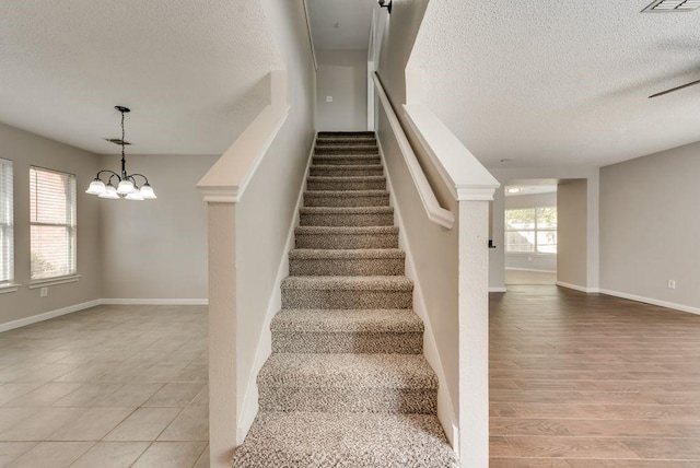 stairs with a textured ceiling and a chandelier