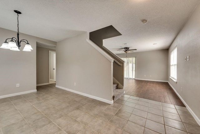 tiled spare room with ceiling fan with notable chandelier and a textured ceiling