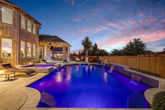 pool at dusk featuring a patio area, a pool with connected hot tub, and a fenced backyard