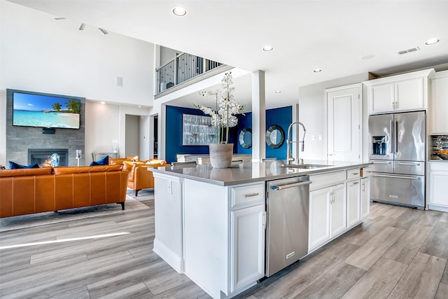 kitchen with visible vents, an island with sink, appliances with stainless steel finishes, a glass covered fireplace, and a sink