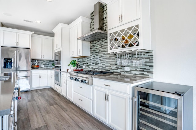 kitchen featuring beverage cooler, white cabinets, stainless steel appliances, and wall chimney range hood