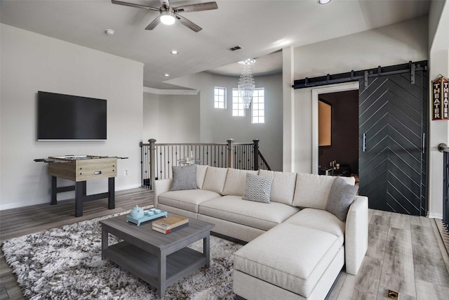 living room with baseboards, a barn door, recessed lighting, ceiling fan with notable chandelier, and wood finished floors