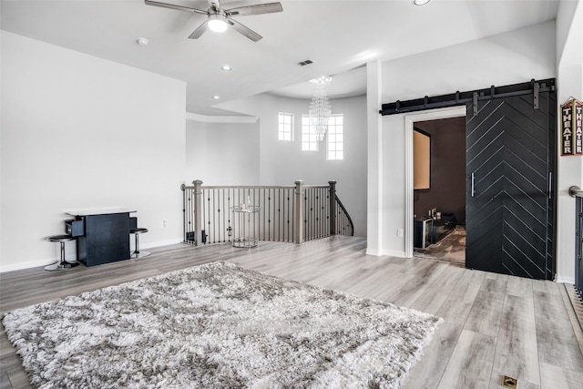 interior space featuring a barn door, an upstairs landing, ceiling fan with notable chandelier, a wood stove, and wood finished floors