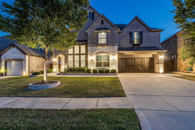 french provincial home with brick siding, stone siding, concrete driveway, and a front yard