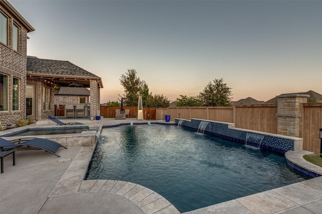 pool at dusk featuring outdoor dry bar, a fenced in pool, a fenced backyard, a patio area, and a ceiling fan