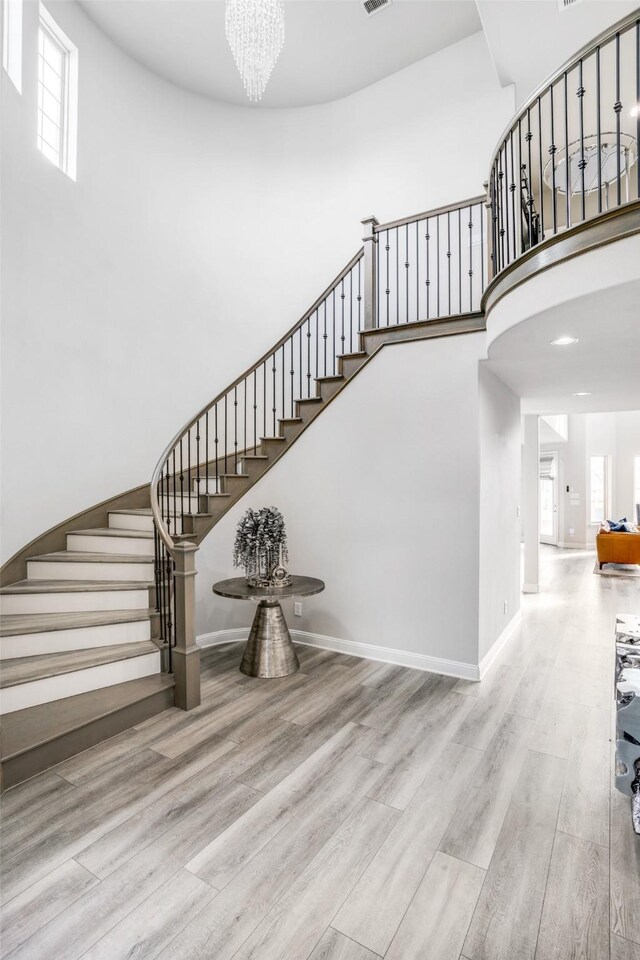 stairs featuring visible vents, baseboards, wood finished floors, and a towering ceiling