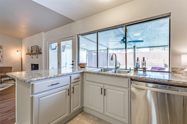 kitchen featuring sink, white cabinets, light tile patterned floors, stainless steel dishwasher, and a brick fireplace